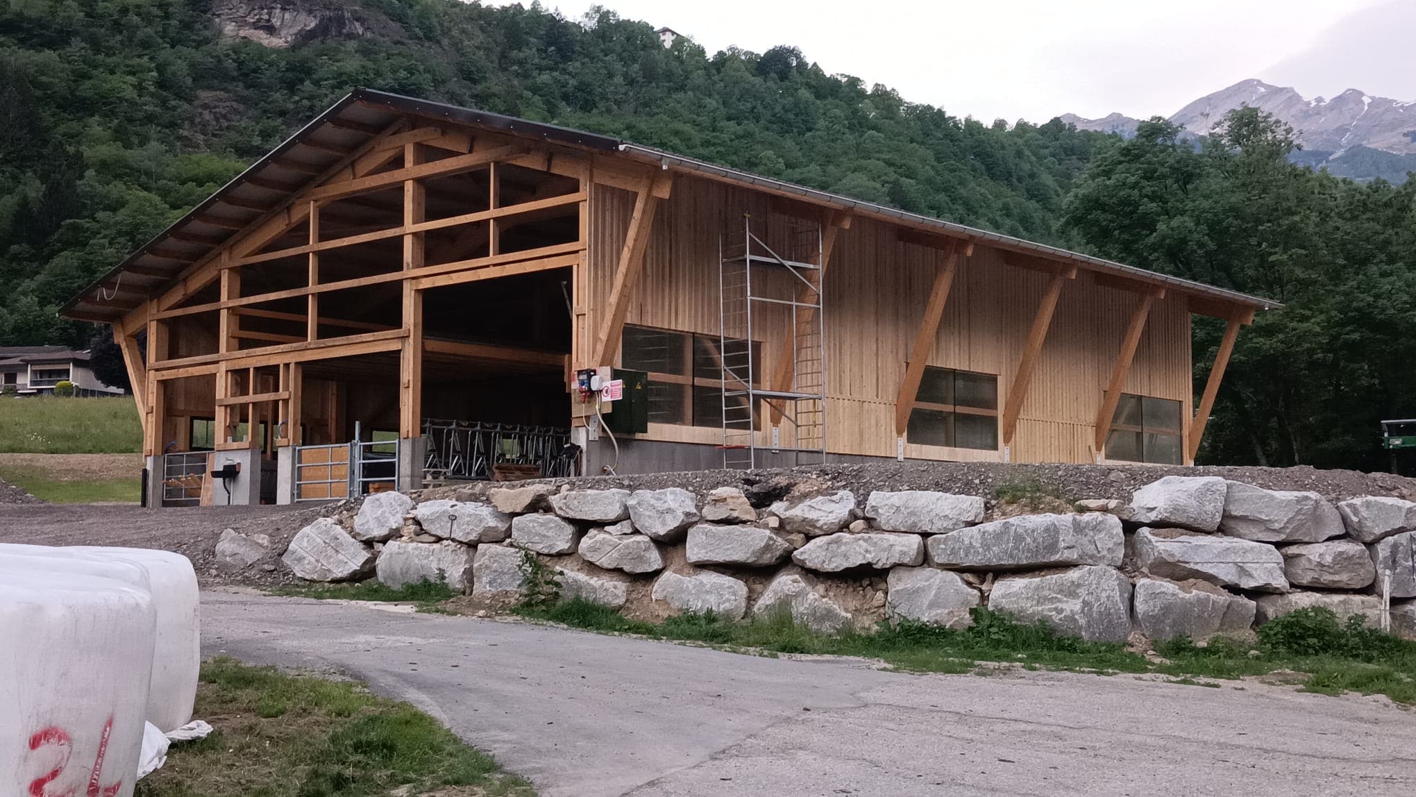 Large timber agricultural hall with Swiss Alps in the background — a completed Bâtiferme project