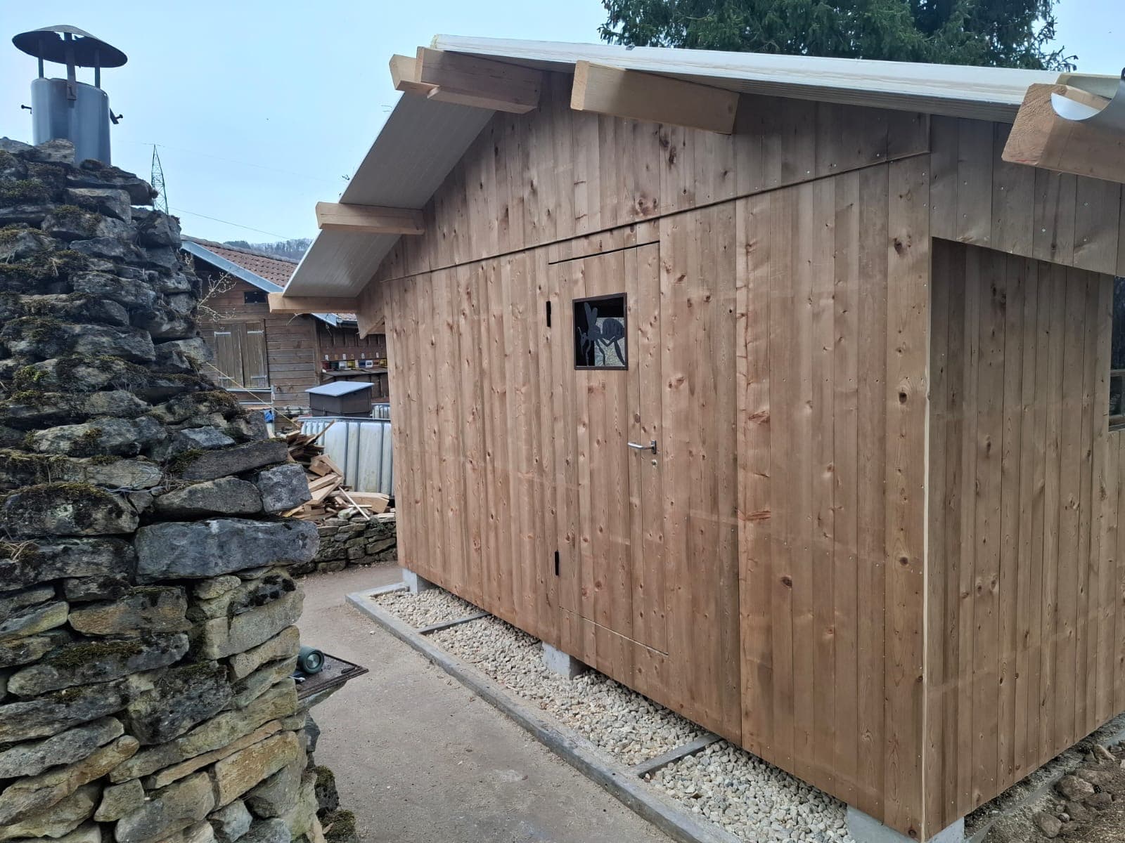 Timber outbuilding next to a traditional stone wall, natural wood cladding