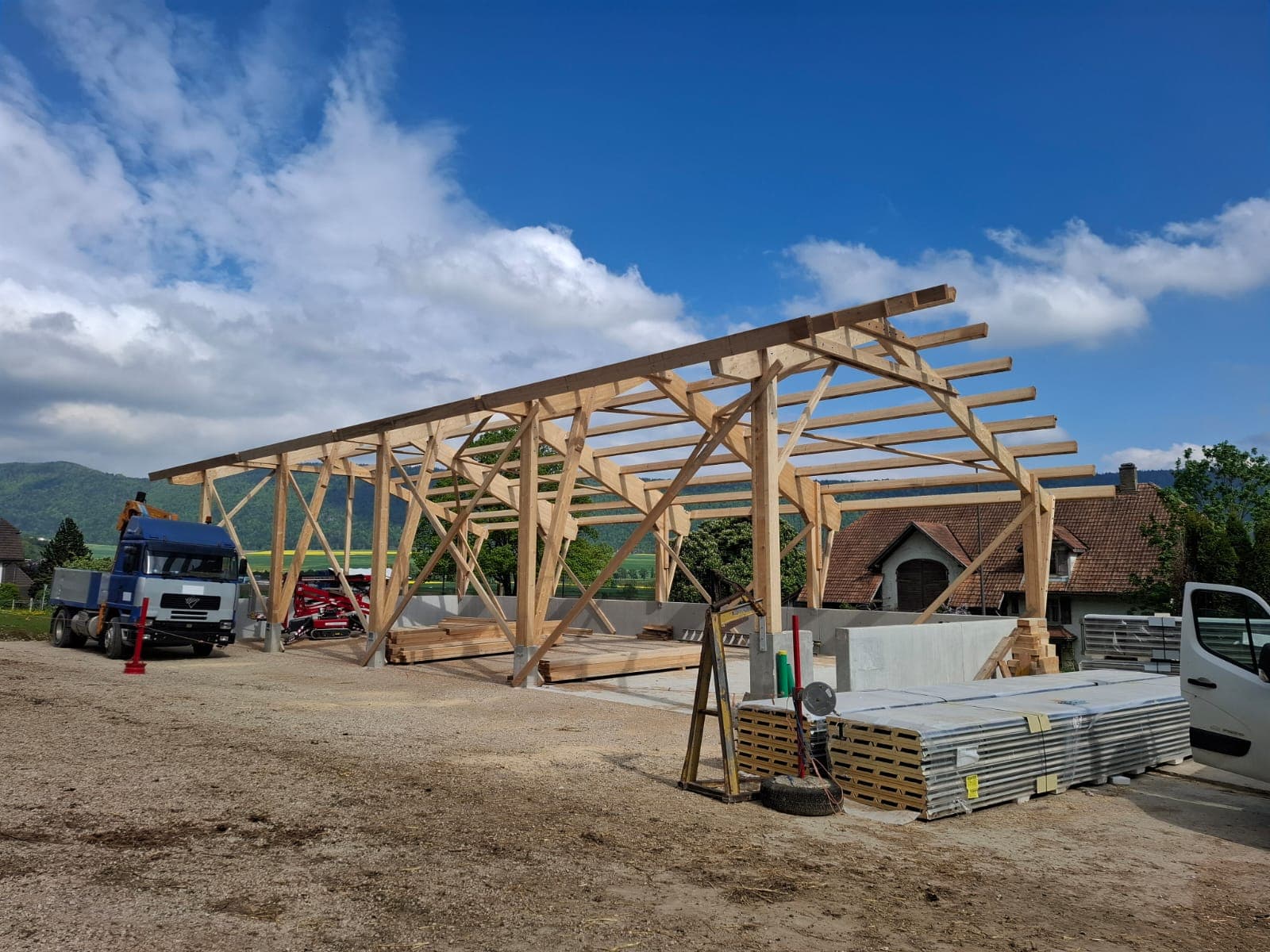 Large timber frame hall skeleton under construction, blue sky and rolling Swiss landscape