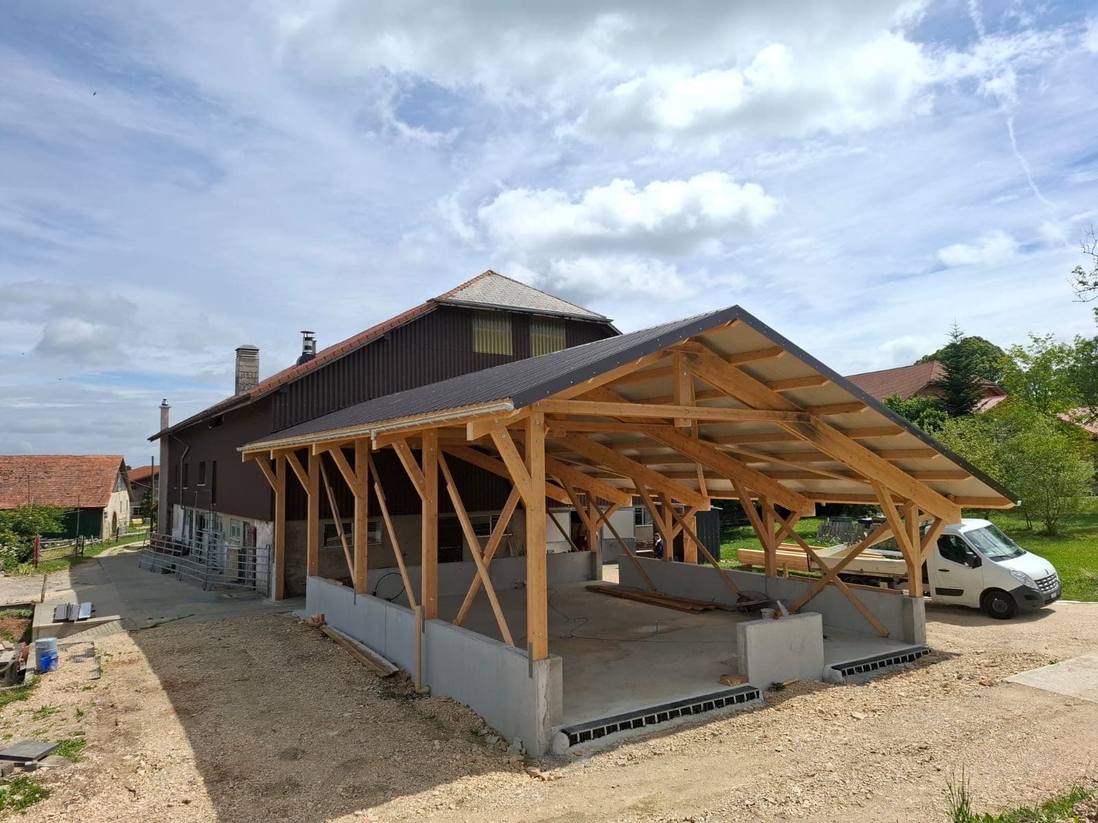 Open timber frame structure under construction in a Swiss rural setting